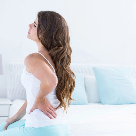 Woman sitting on a bed with one hand on her lower back